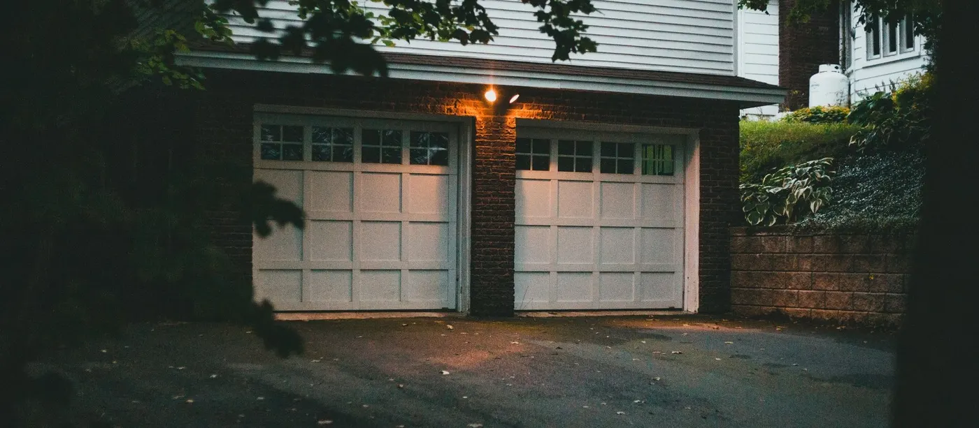 Double garage door on a brick home lit by a porch light at dusk