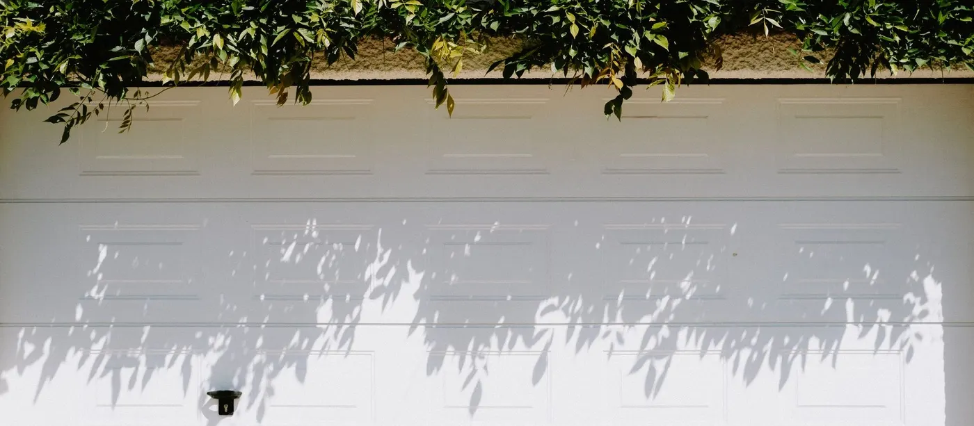 Closed white sectional garage door with leaf shadows across the panels