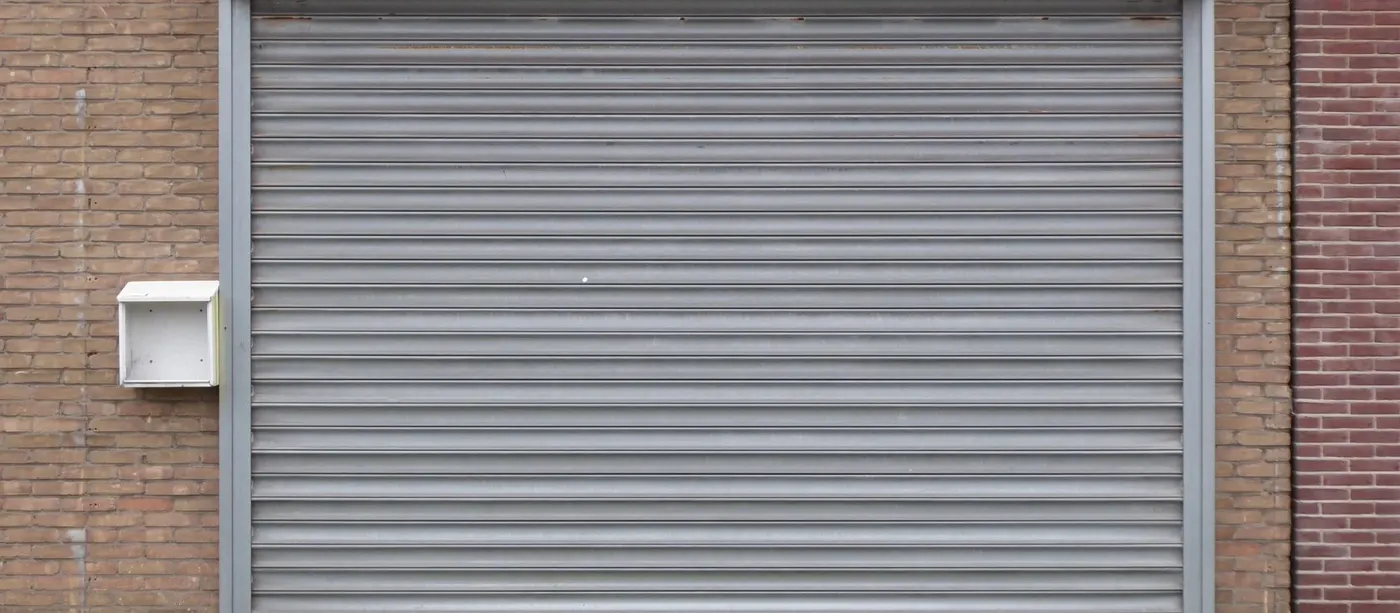 Closed grey metal roller door on a brick garage